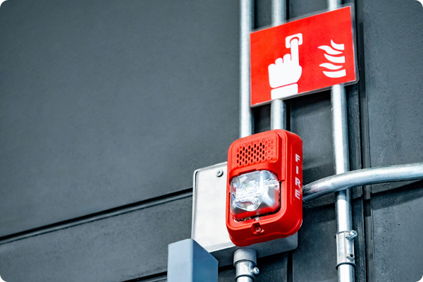 5-	Zdjęcie elementów systemu bezpieczeństwa przeciwpożarowego. Urządzenia zamontowane są na jasnej ścianie i stanowią wyposażenie systemu reagowania na sytuacje awaryjne.
