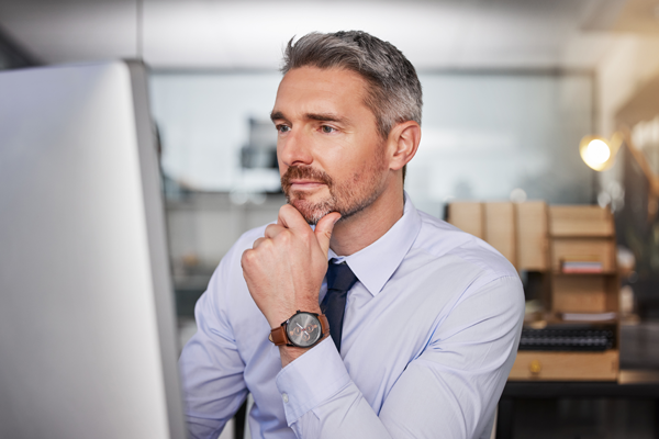 Mężczyzna w biurze sprawdza na ekranie komputera swoją fakturę za prąd.