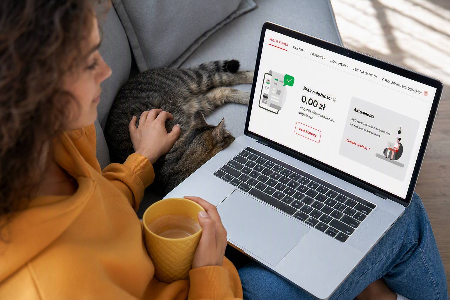 Kobieta siedzi na kanapie z laptopem na kolanach, w prawym ręku trzyma kubek, obok leży kot. Na ekranie laptopa widok po zalogowanie do serwisu Energa24.
