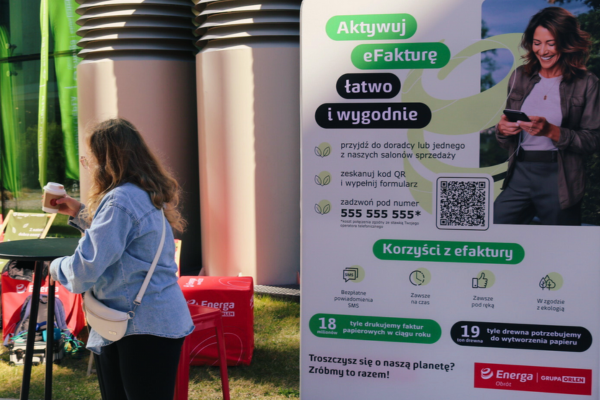 Kobieta na wydarzeniu promującym eFakturę. W tle baner reklamowy zachęcający do aktywacji eFaktury.
