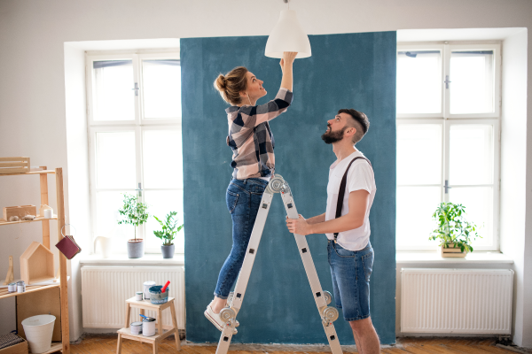Para wspólnie montująca lampę wiszącą w nowo urządzanym mieszkaniu.