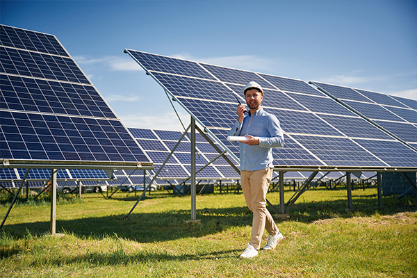 Osoba stojąca na trawie obok dużej instalacji paneli fotowoltaicznych