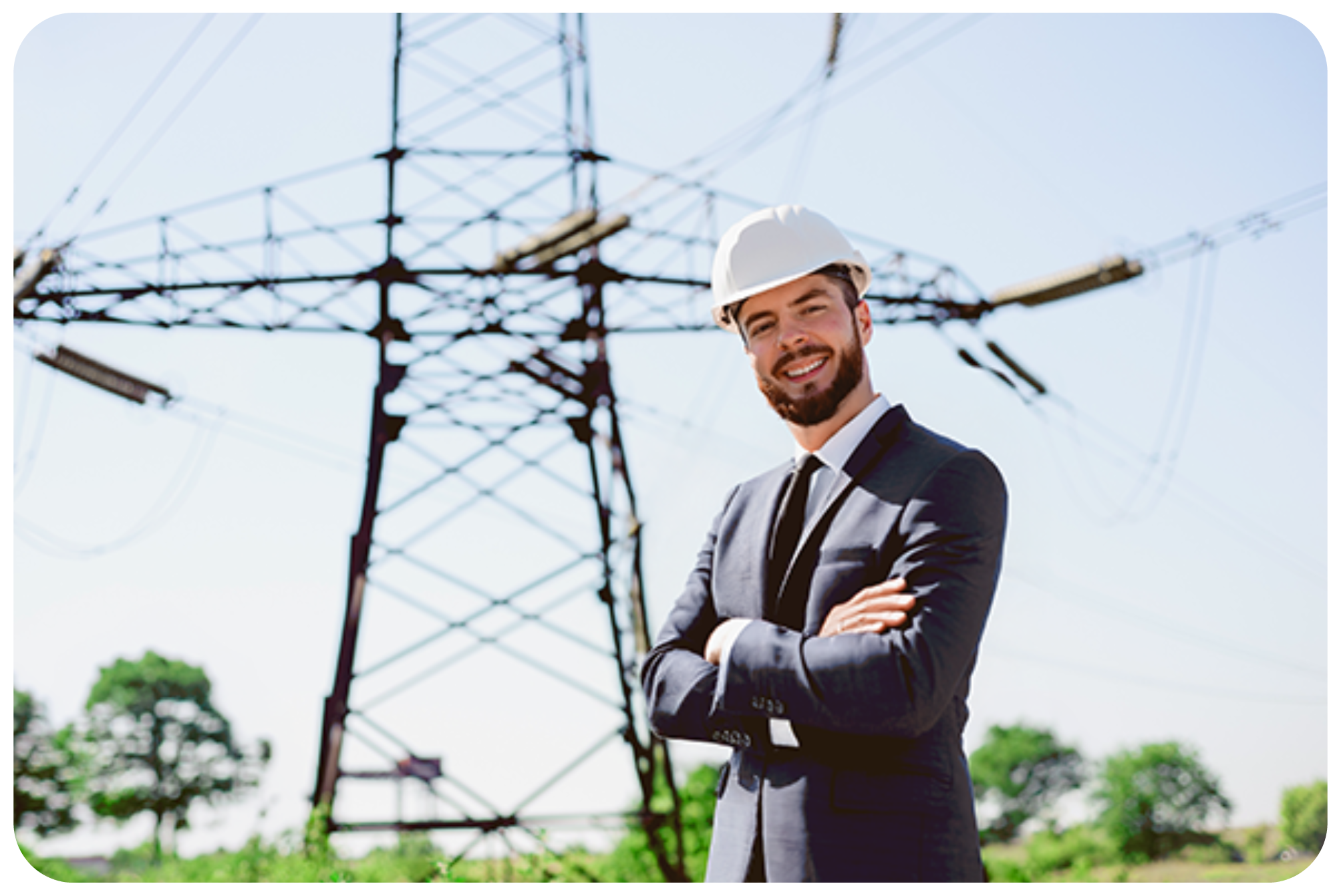 Uśmiechnięty inżynier w kasku ochronnym stoi na tle infrastruktury elektroenergetycznej wysokiego napięcia.
